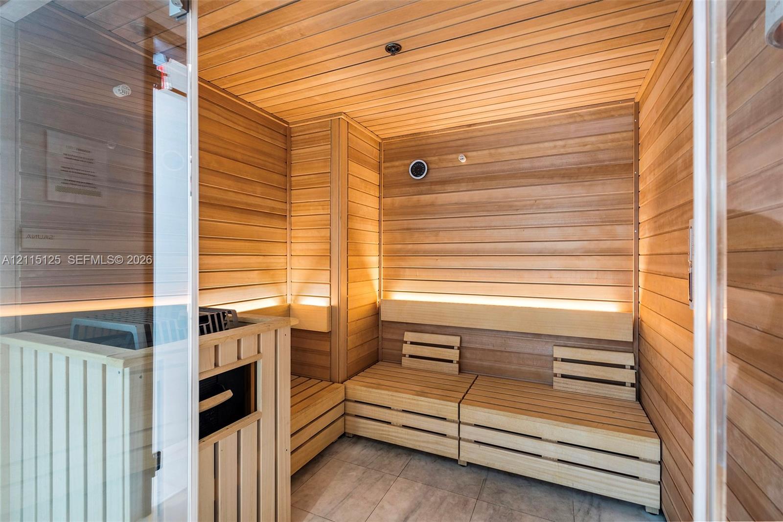Sauna featuring natural wood tongue-and-groove wall paneling, integrated recessed LED accent lighting, multi-level wooden bench seating, and a glass-paneled entrance