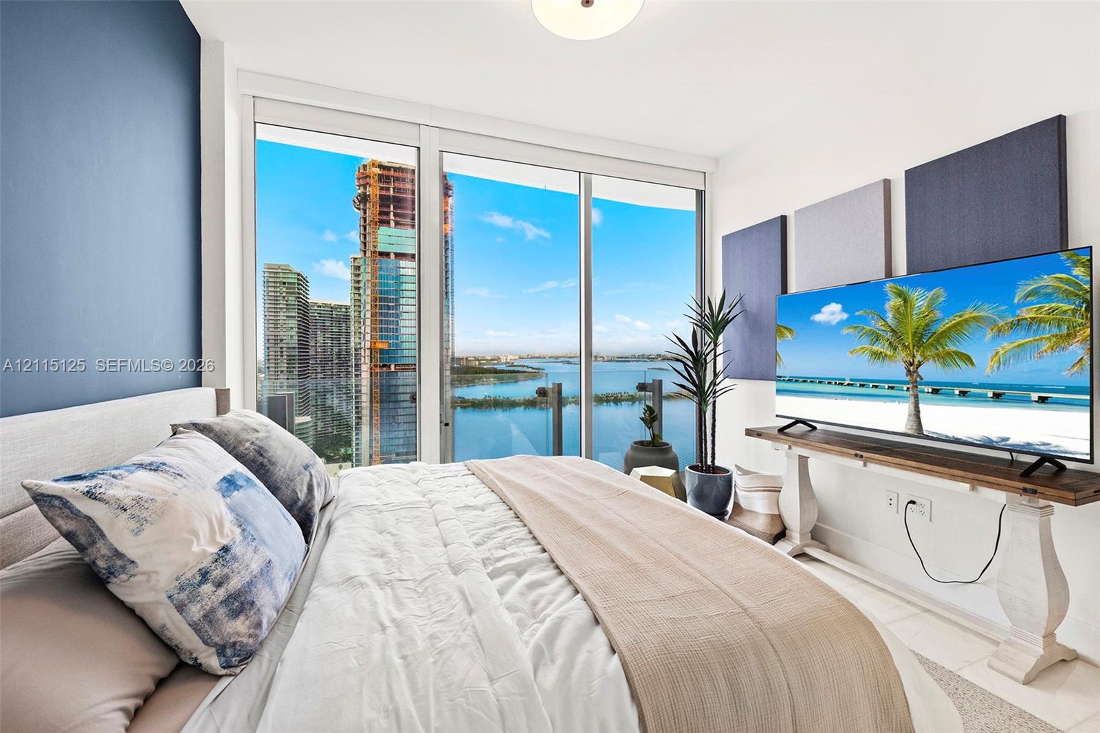 Floor-to-ceiling windows, blue accent wall, neutral tile flooring, and a private balcony