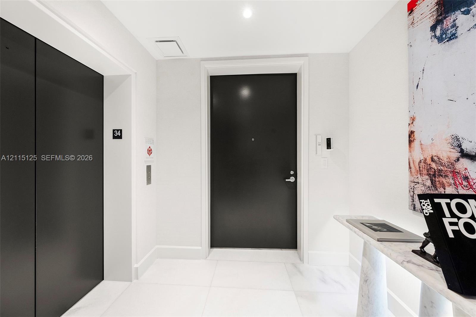 Entryway featuring large-format light tile flooring, solid-core matte black door with integrated hardware, private elevator access, and recessed ceiling lighting