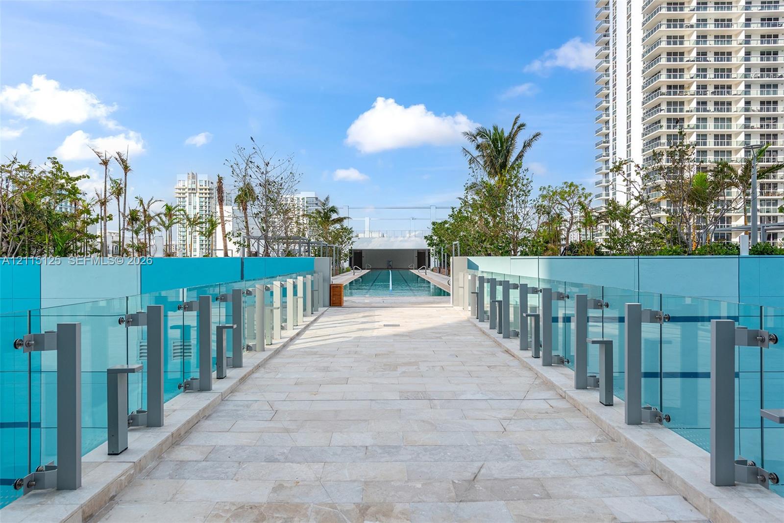 Elevated stone-paved promenade featuring glass panel railings, integrated pathway lighting, and lap pool access