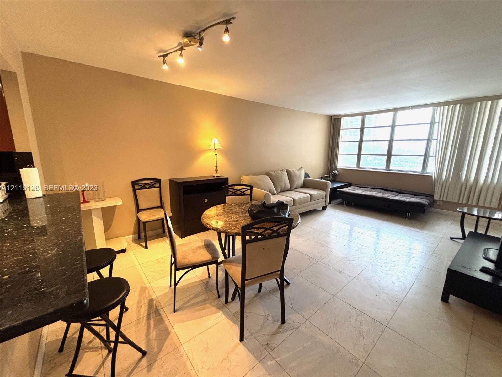 Open floor plan featuring large format tile flooring, a breakfast bar with dark stone countertop, and an expansive window wall Open floor plan featuring large format tile flooring, a breakfast bar with dark stone countertop, and an expansive window wall
