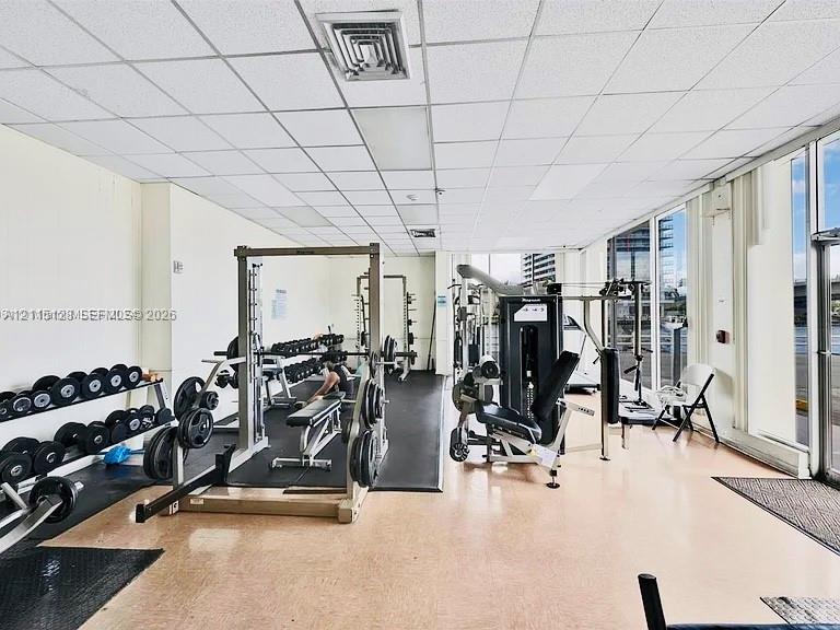Fitness center featuring floor-to-ceiling windows, rubberized flooring, and drop ceiling panels Fitness center featuring floor-to-ceiling windows, rubberized flooring, and drop ceiling panels