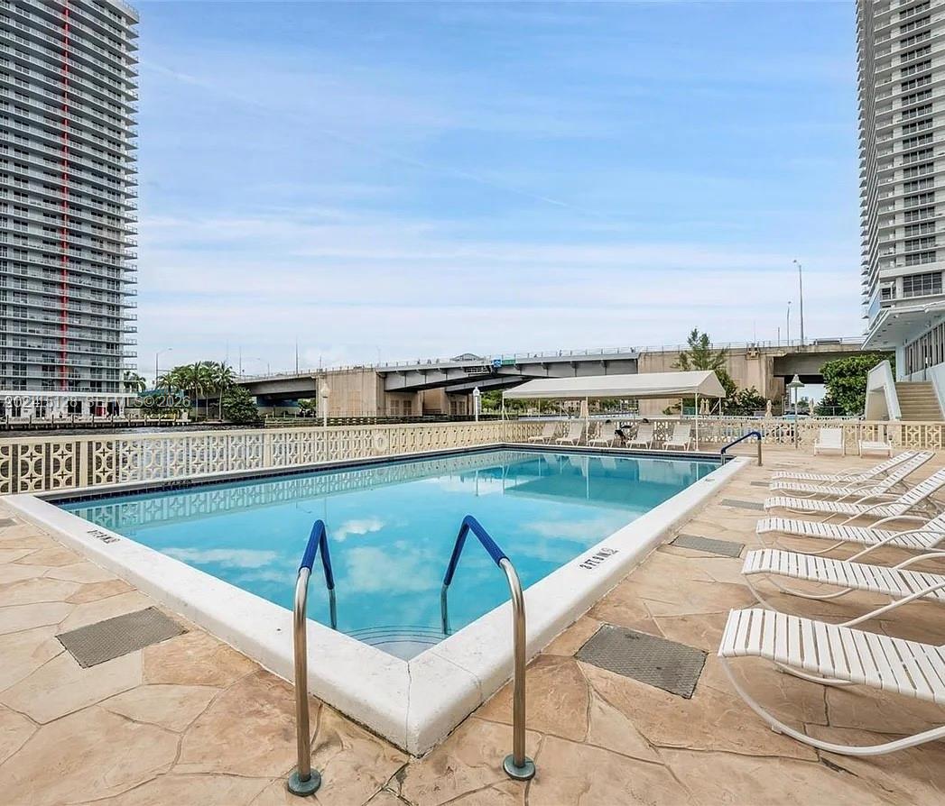Outdoor swimming pool featuring a concrete deck, decorative perimeter screen, and metal handrails