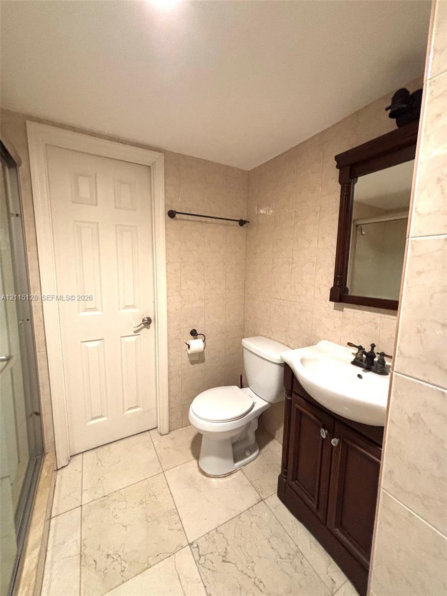 Bathroom featuring full-height stone-finish wall tile, large-format floor tile, dark wood-finish vanity with a white basin, oil-rubbed bronze fixtures, and a framed wall mirror