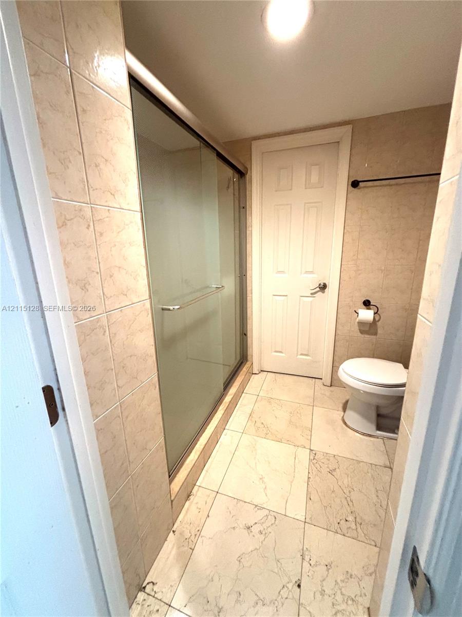 Walk-in shower with sliding glass doors, large-format tile flooring, neutral wall tiling, and a white interior door