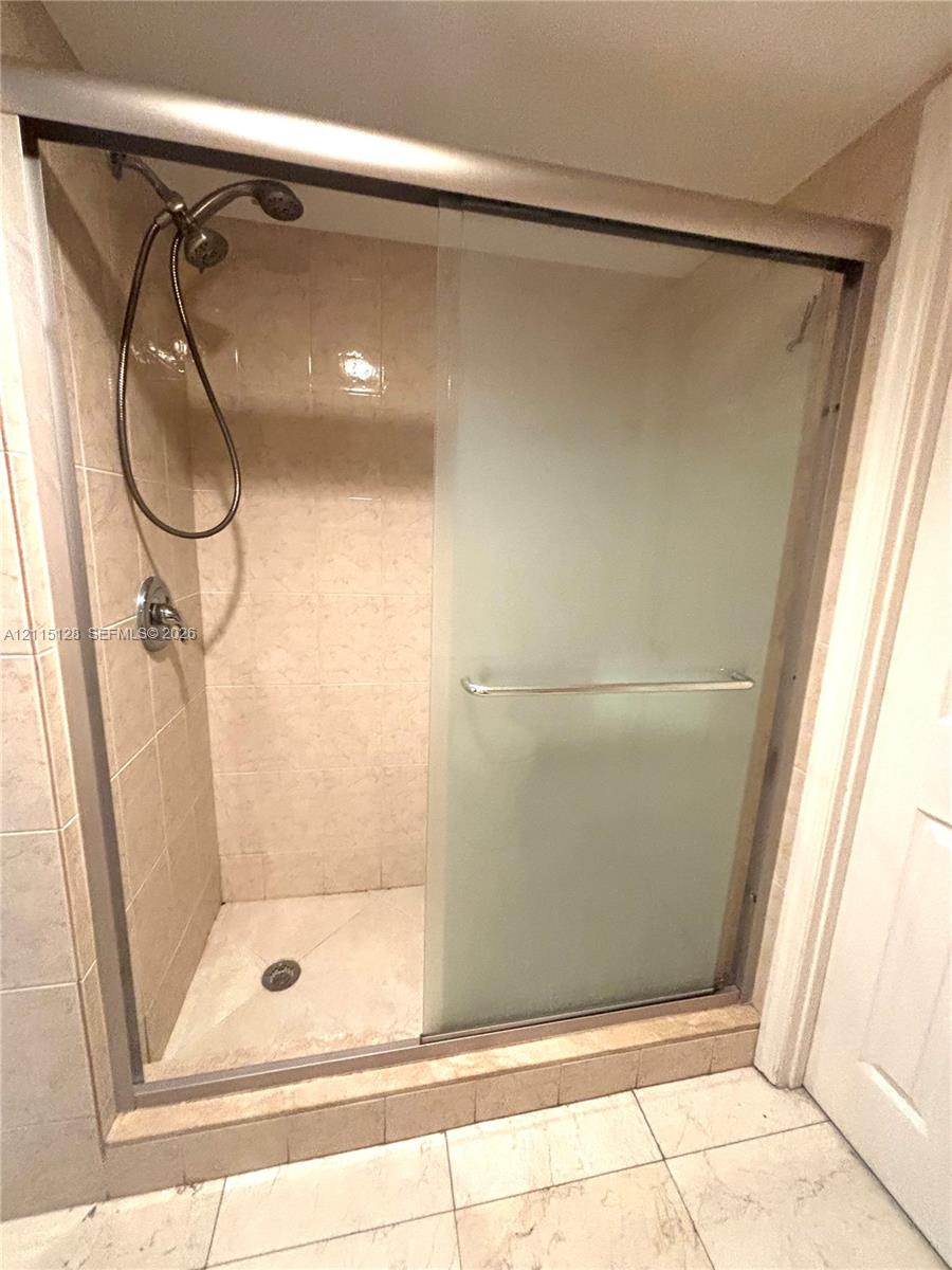Walk-in shower enclosure featuring floor-to-ceiling tile, a frosted glass sliding door, metallic hardware, and a handheld showerhead Walk-in shower enclosure featuring floor-to-ceiling tile, a frosted glass sliding door, metallic hardware, and a handheld showerhead