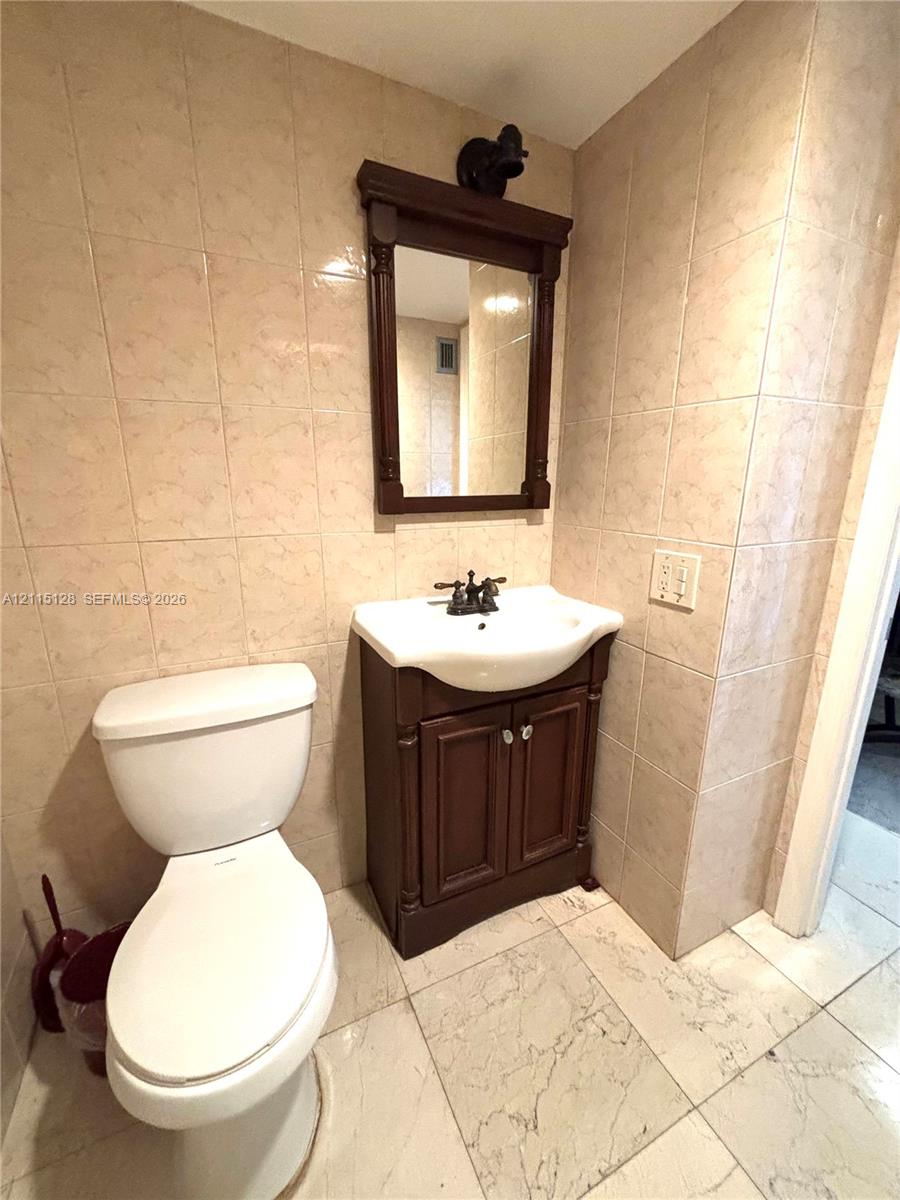 Bathroom featuring tile wall surround, vanity cabinet with a porcelain sink, dual-handle faucet, and framed wall-mounted mirror