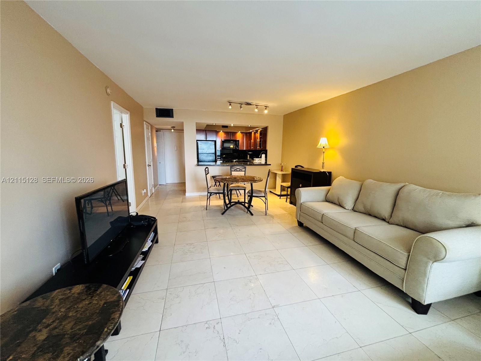 Interior featuring large-format light-toned tile flooring, recessed kitchen cabinetry, track lighting, and a kitchen pass-through opening Interior featuring large-format light-toned tile flooring, recessed kitchen cabinetry, track lighting, and a kitchen pass-through opening