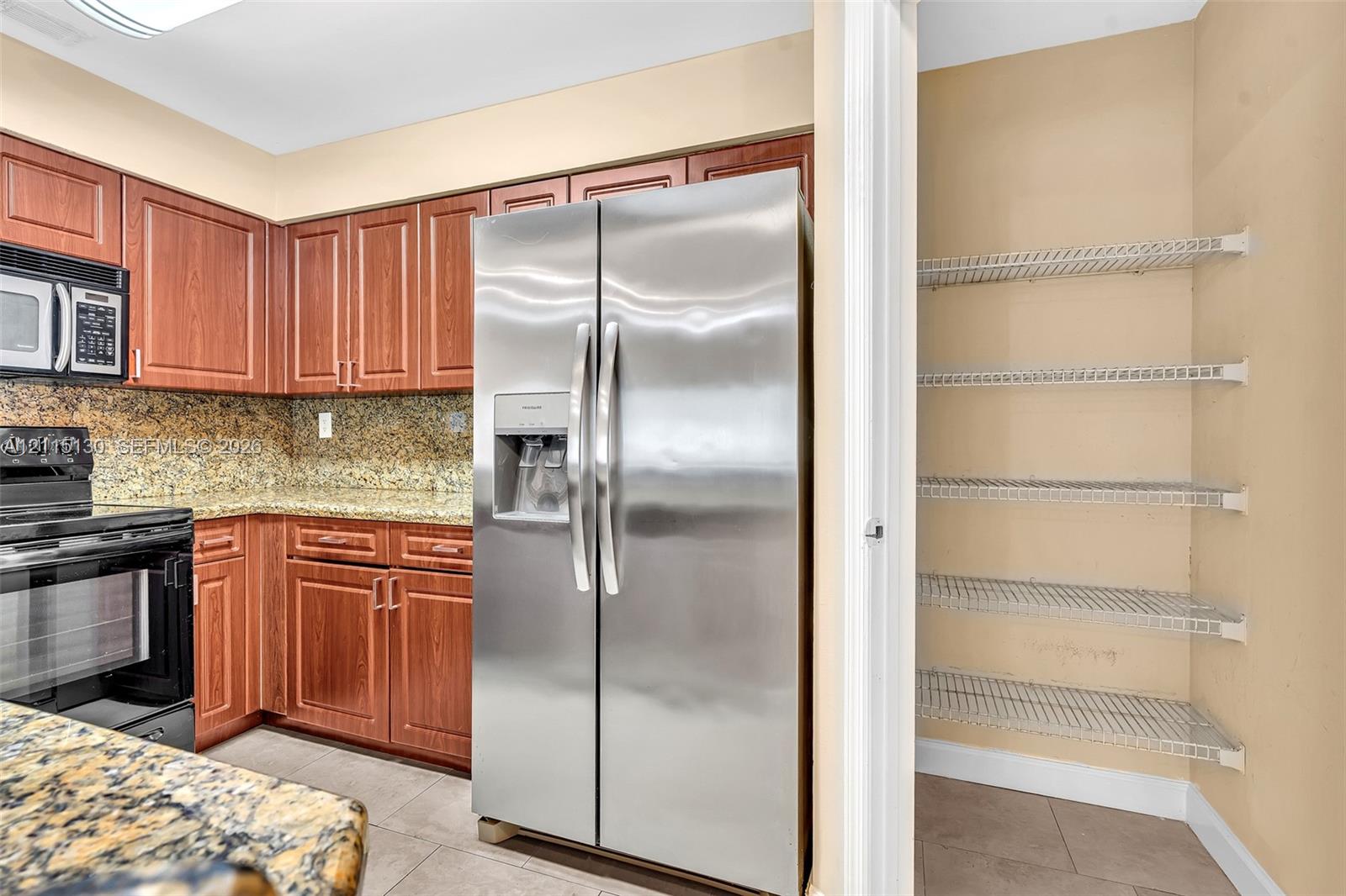 Kitchen featuring wood cabinetry, stone-surface countertops, stainless steel appliances, and a built-in wire shelving pantry