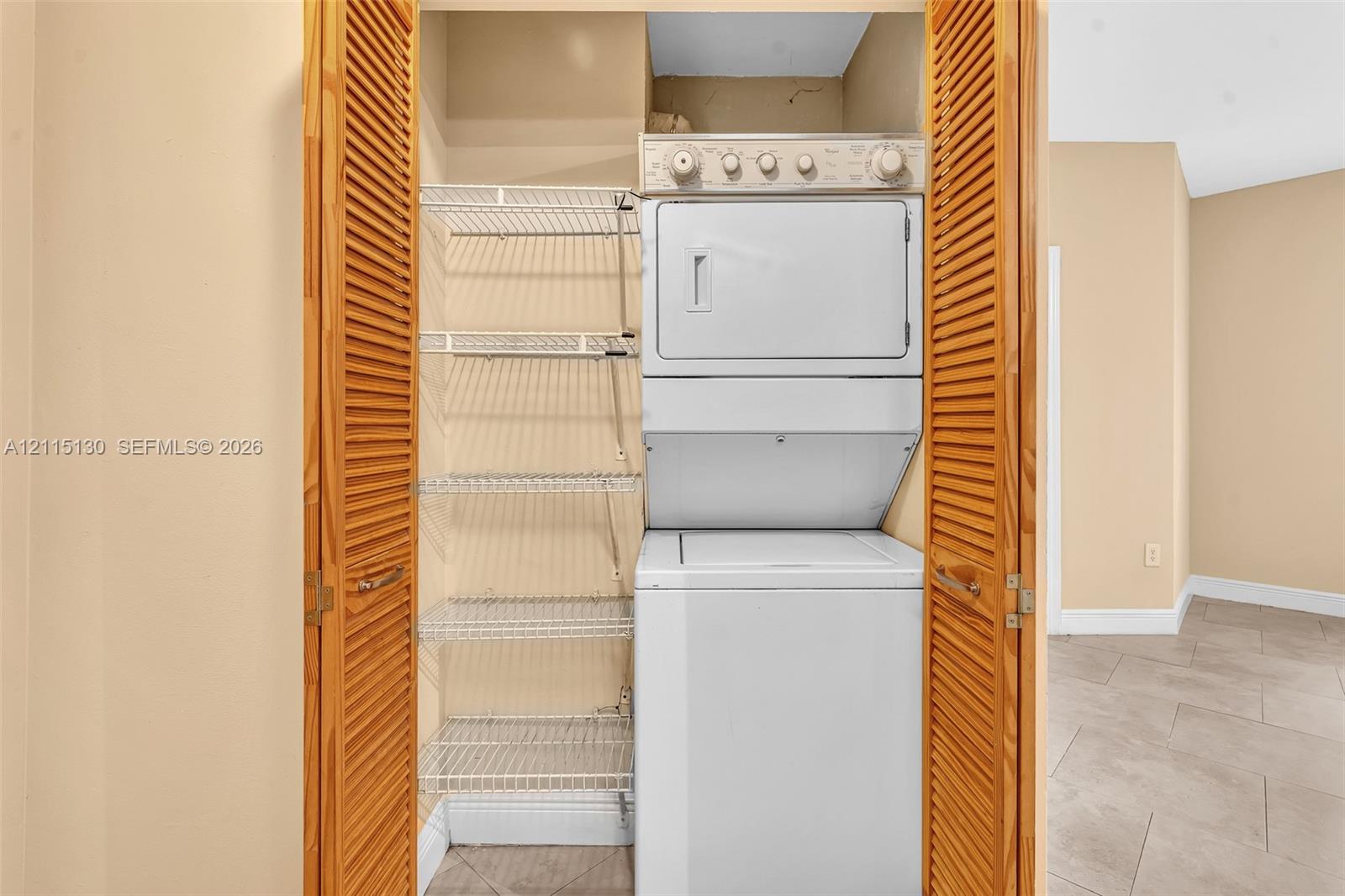 Laundry closet featuring louvered wooden doors, a stacked washer and dryer unit, and built-in wire shelving