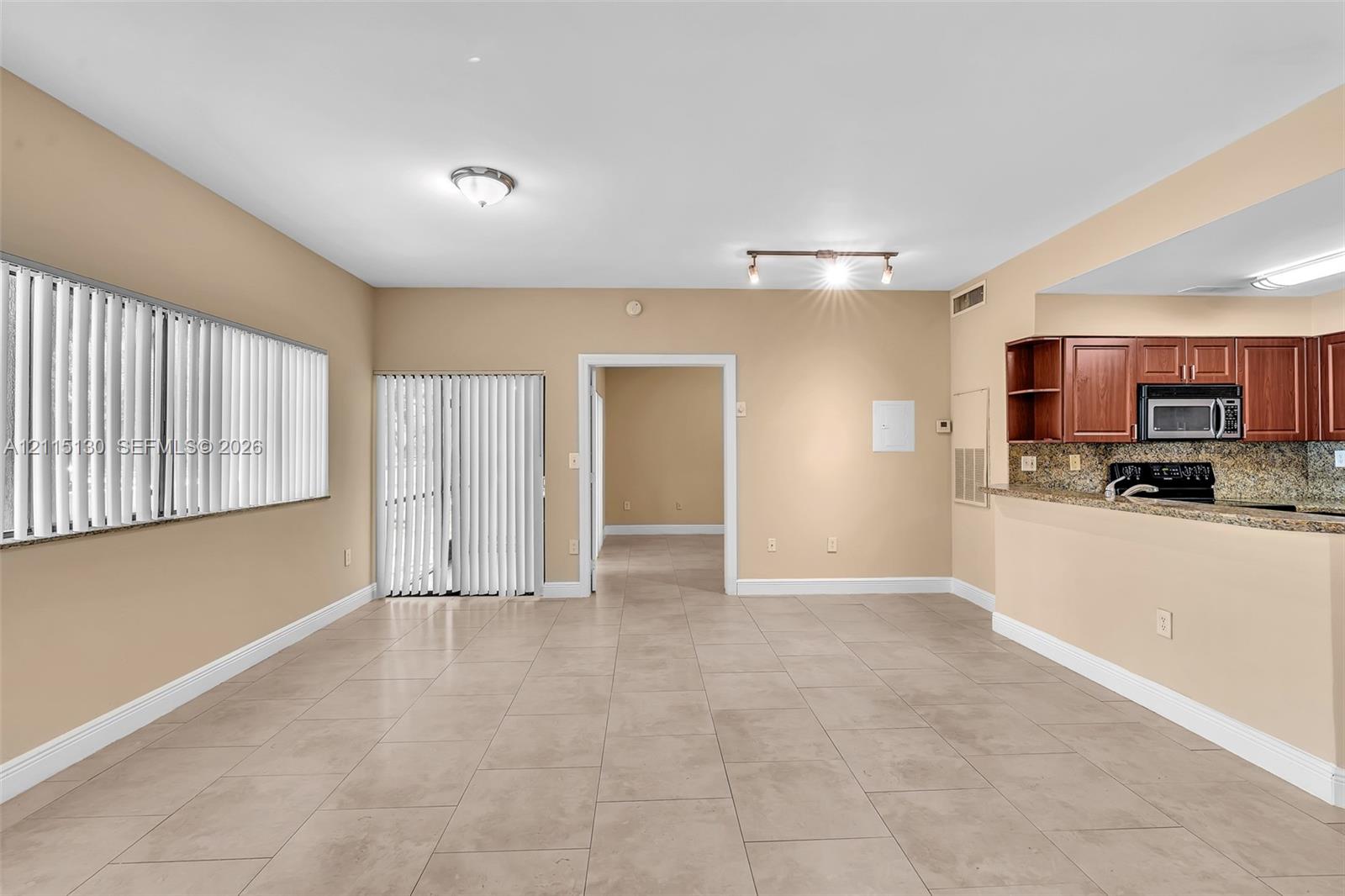 Large-format tile flooring, kitchen featuring wood-finish cabinetry, stone-surface countertops, track lighting, and sliding glass door