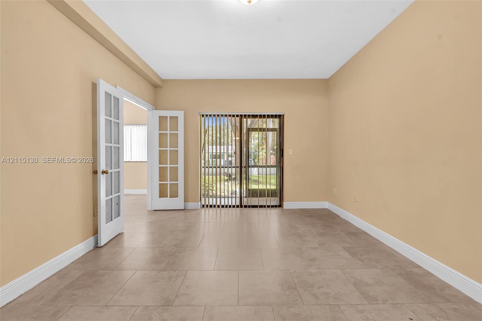 Interior space featuring neutral wall paint, large-format tile flooring, white-framed French doors, and sliding glass doors with vertical blinds