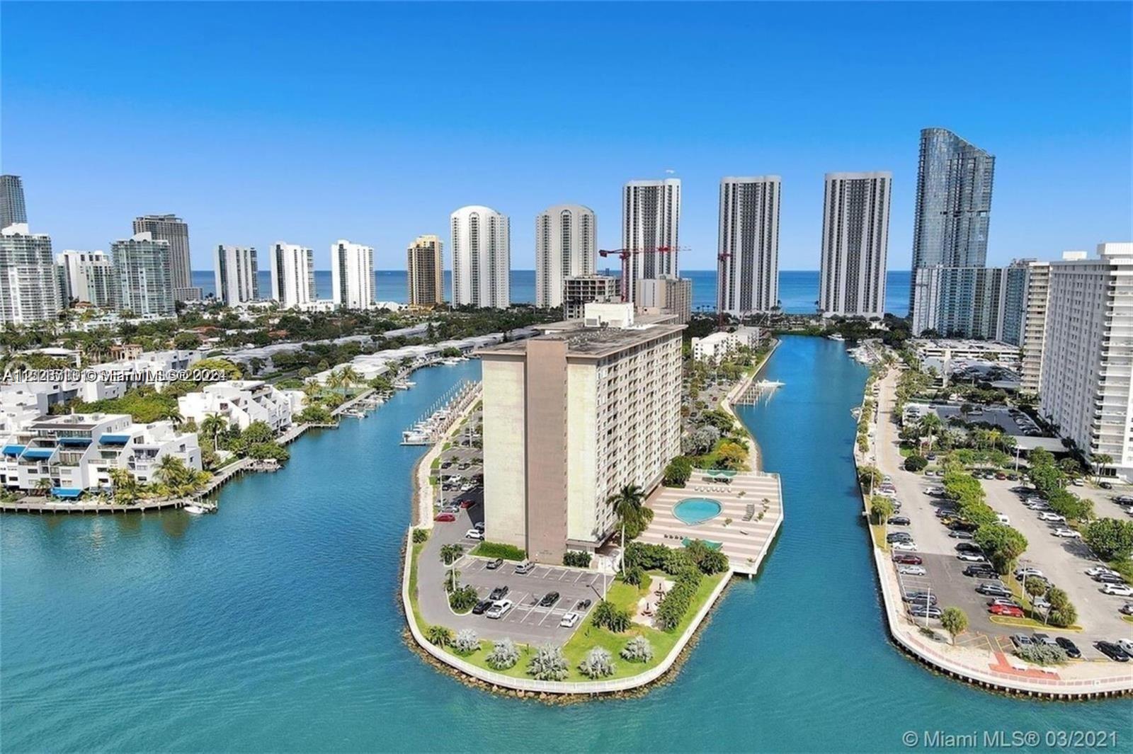 Waterfront high-rise building situated on a peninsula, featuring a ground-level swimming pool, paved sundeck, boat slips, and surface parking Waterfront high-rise building situated on a peninsula, featuring a ground-level swimming pool, paved sundeck, boat slips, and surface parking