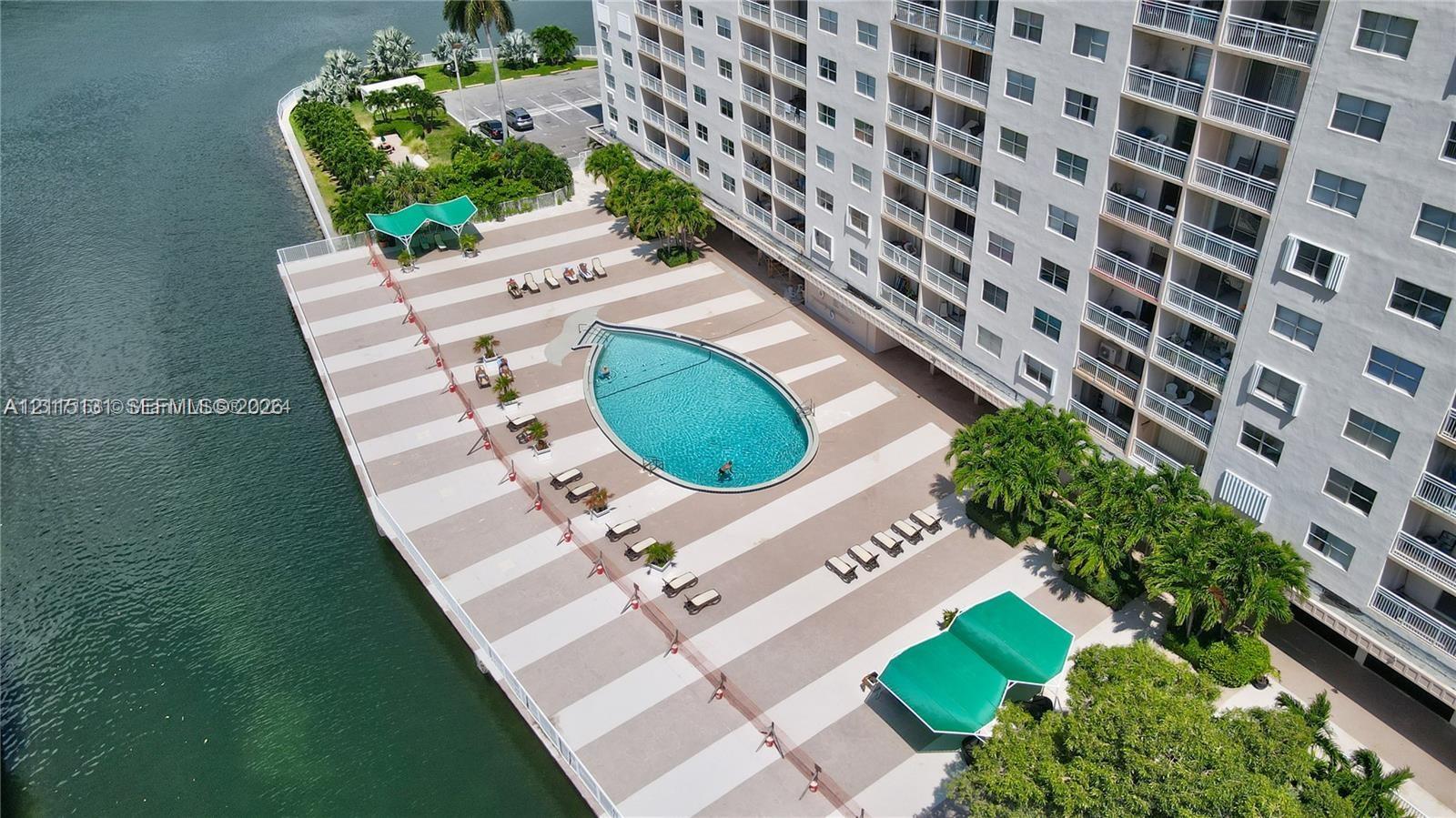 Waterfront swimming pool featuring a paved pool deck, custom shade structures, and mature landscaping Waterfront swimming pool featuring a paved pool deck, custom shade structures, and mature landscaping