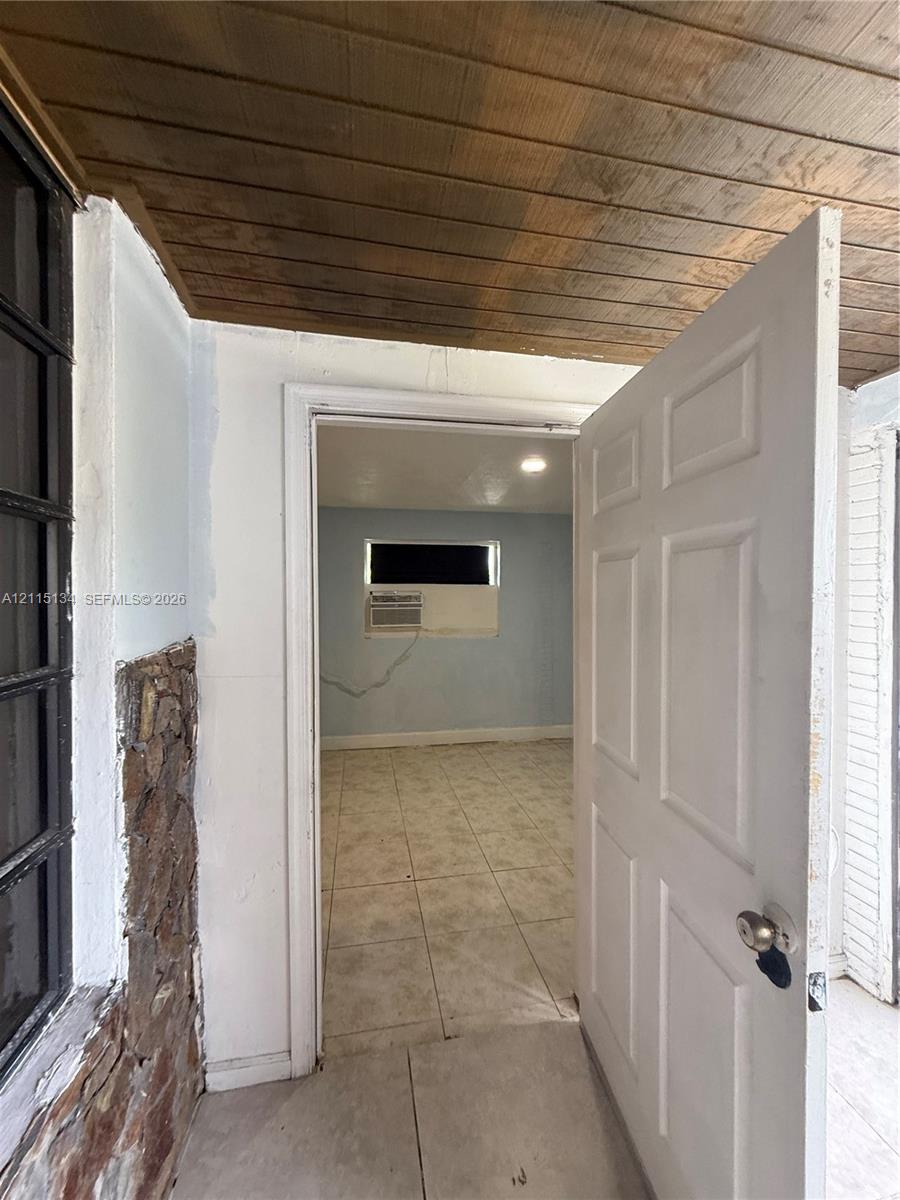Exterior entry area featuring a natural stone accent wall, wood-plank ceiling, and tile flooring
