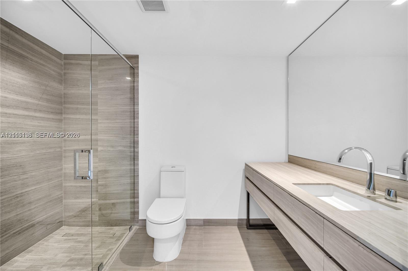 Floating vanity featuring a wood-finish cabinet and integrated sink, full-width wall mirror, glass-enclosed shower with large-format horizontal tile, and polished chrome fixtures