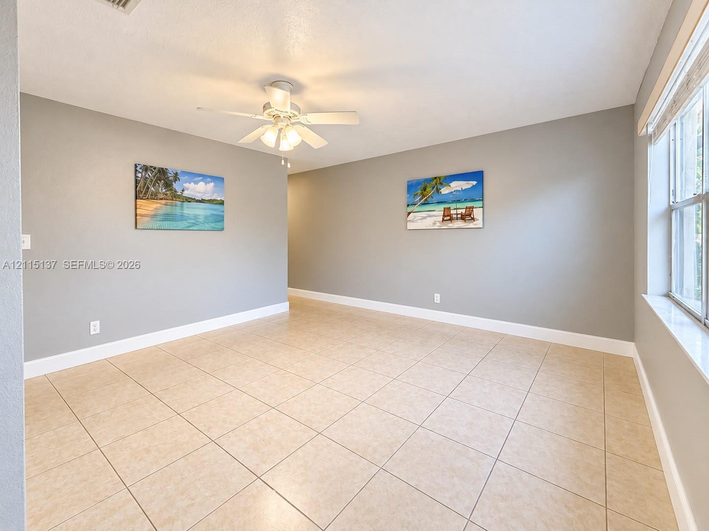 Interior space featuring neutral wall paint, tile flooring, white-finish ceiling fan with integrated lighting, and a multi-pane window Interior space featuring neutral wall paint, tile flooring, white-finish ceiling fan with integrated lighting, and a multi-pane window