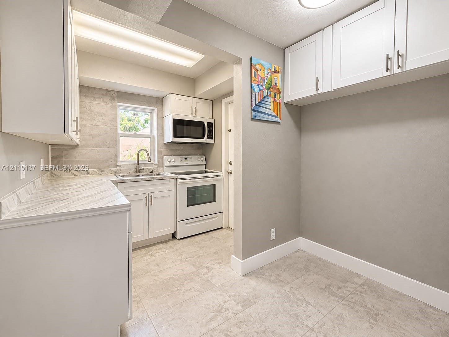 Kitchen featuring white cabinetry, solid-surface countertops, tile backsplash, built-in microwave, and large-format tile flooring Kitchen featuring white cabinetry, solid-surface countertops, tile backsplash, built-in microwave, and large-format tile flooring