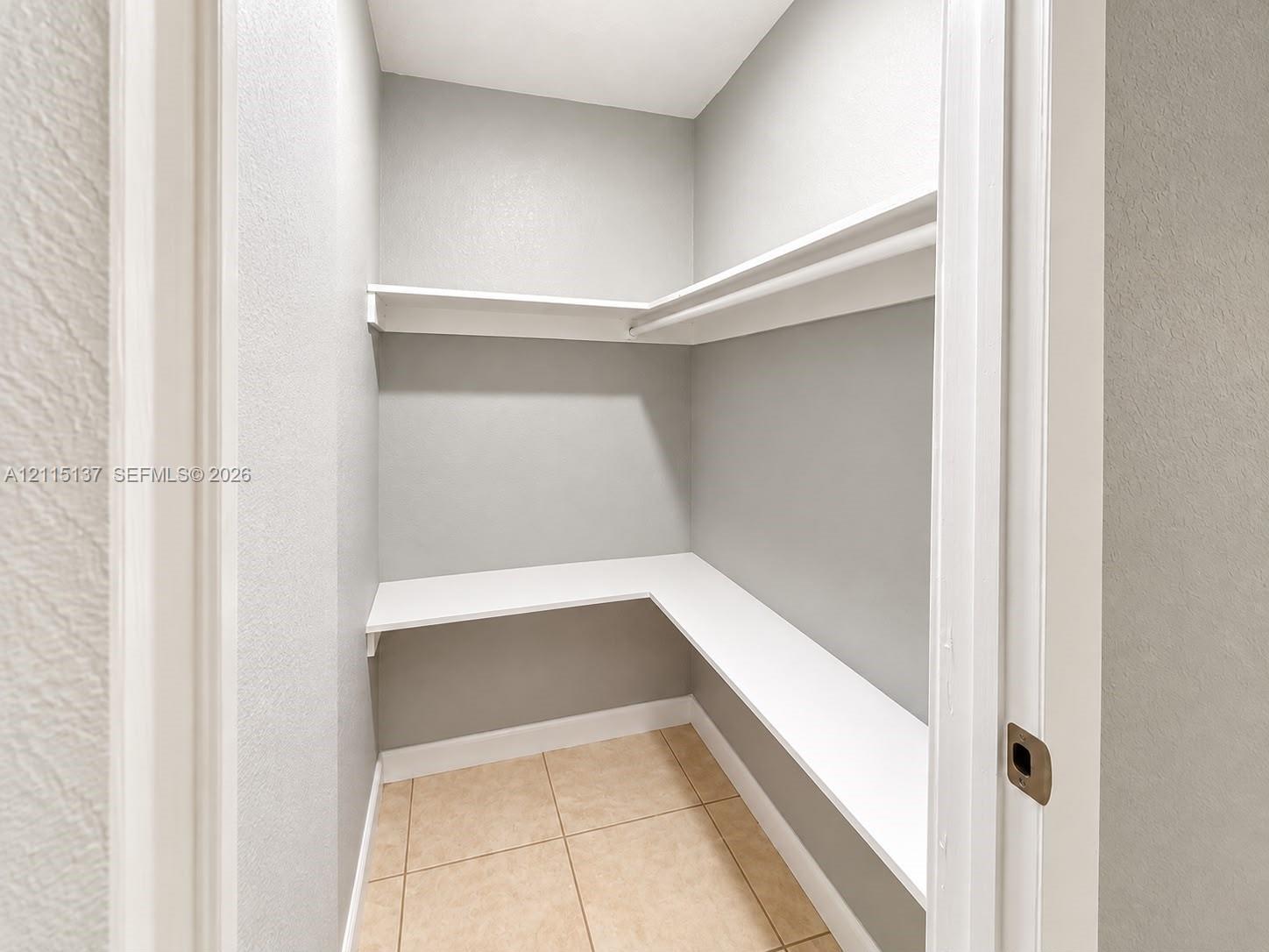 Storage area featuring multi-level wrap-around shelving and neutral tile flooring Storage area featuring multi-level wrap-around shelving and neutral tile flooring