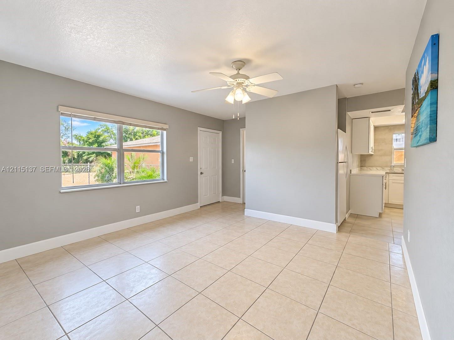 Interior space featuring neutral wall paint, tile flooring, a multi-blade ceiling fan with integrated light fixture, and a large window Interior space featuring neutral wall paint, tile flooring, a multi-blade ceiling fan with integrated light fixture, and a large window