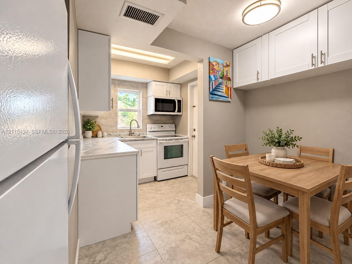 Kitchen featuring white shaker-style cabinetry, stone-patterned countertops, a stainless steel sink with a gooseneck faucet, an integrated over-the-range microwave, and light-toned ceramic tile flooring
