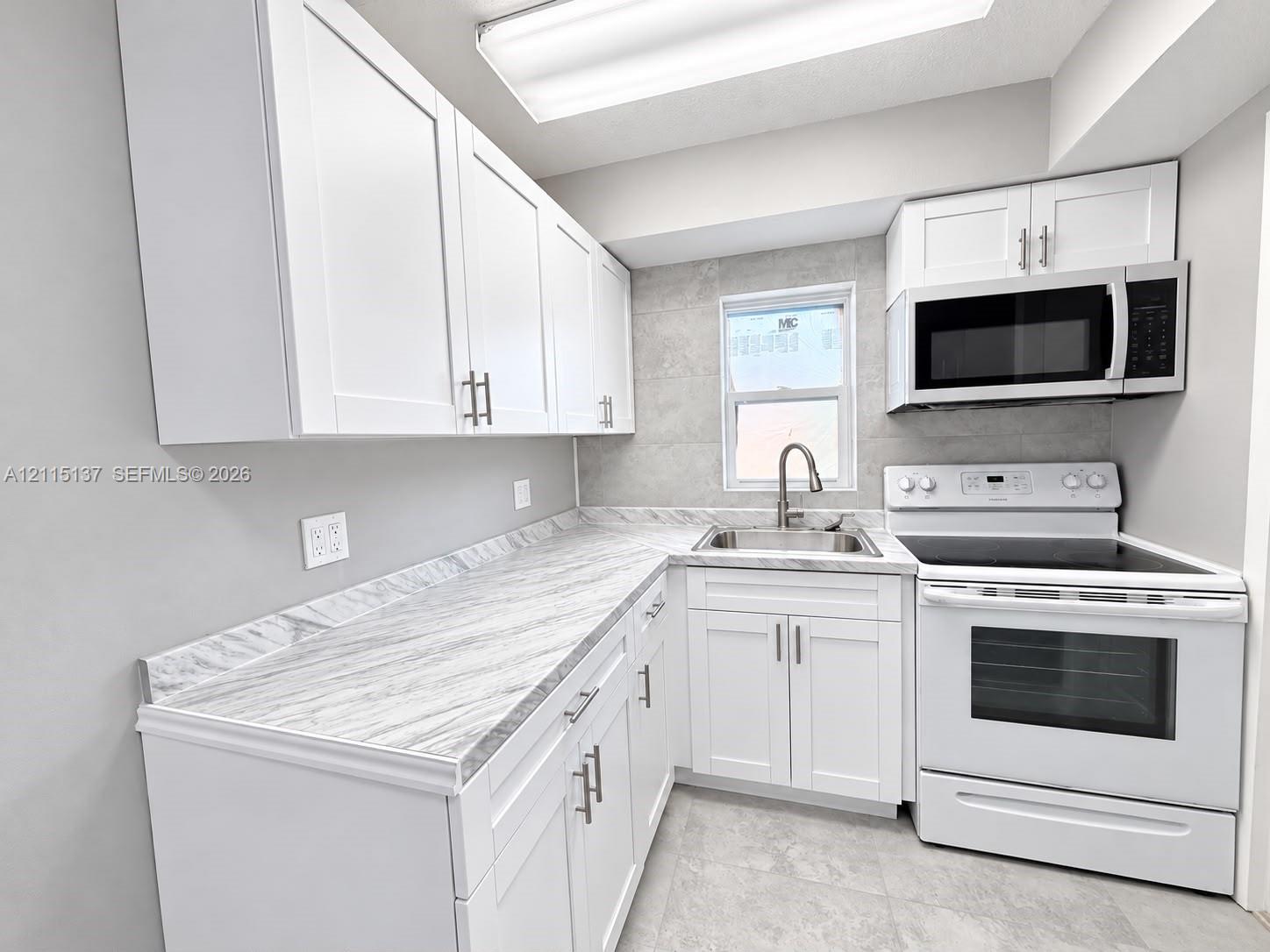Kitchen featuring white shaker-style cabinetry, stone-patterned laminate countertops, stainless steel sink with pull-down faucet, white electric range with built-in microwave, and large-format tile backsplash Kitchen featuring white shaker-style cabinetry, stone-patterned laminate countertops, stainless steel sink with pull-down faucet, white electric range with built-in microwave, and large-format tile backsplash