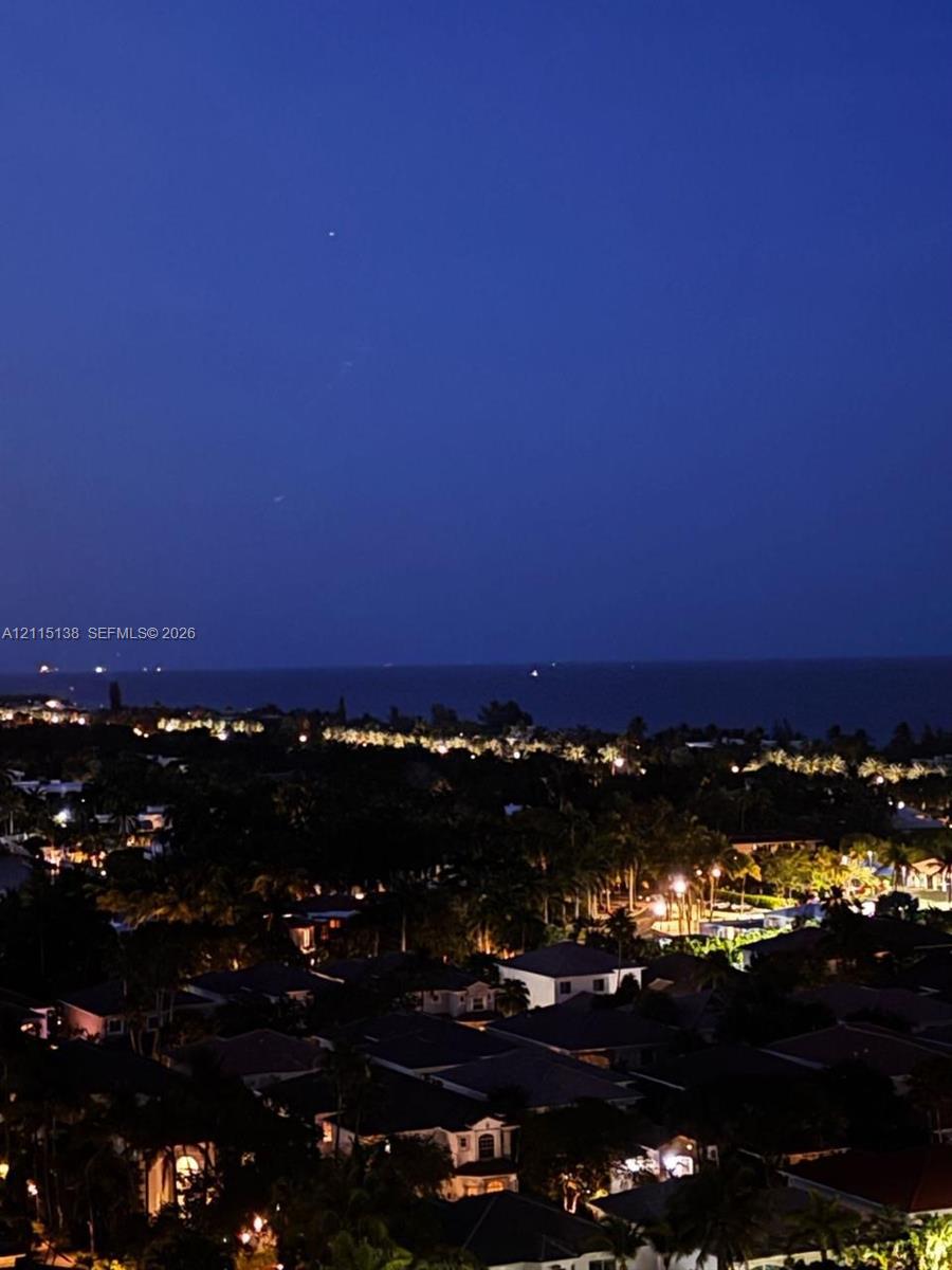 Elevated perspective of the coastal landscape featuring expansive water horizon and illuminated residential area