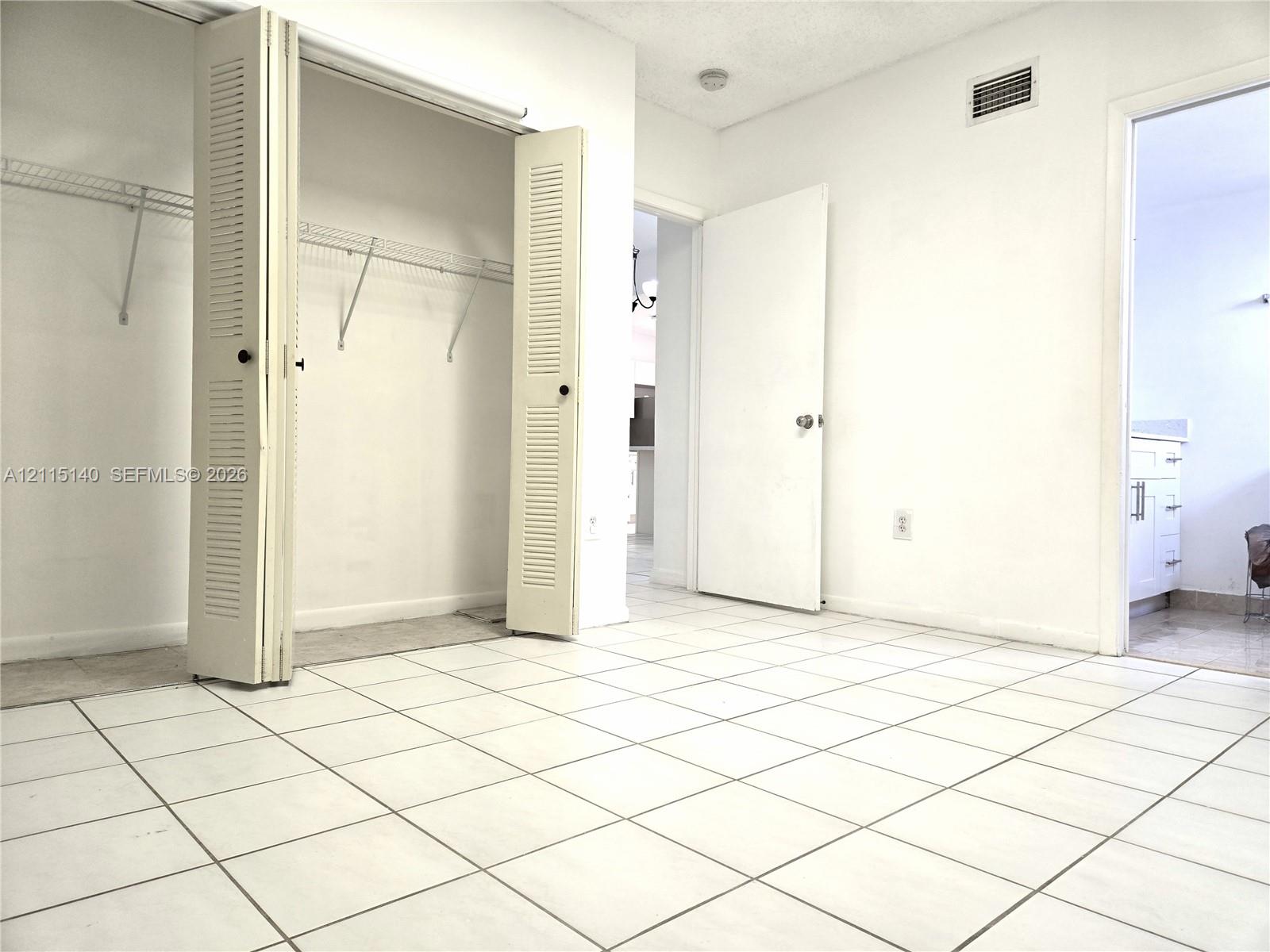 Neutral tile flooring, built-in dual-panel louvered closet doors, and wire shelving