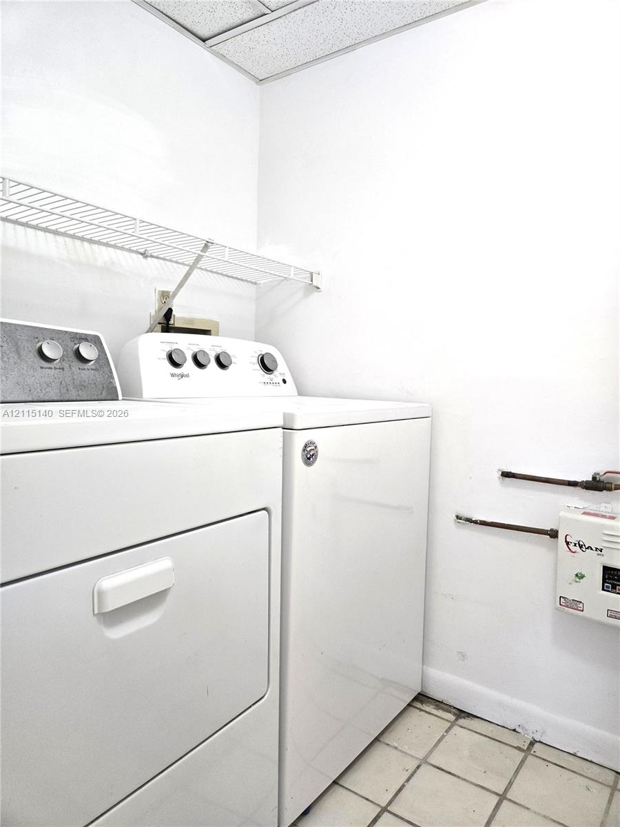 Utility area featuring white built-in laundry appliances, wire wall-mounted shelving, and tile flooring