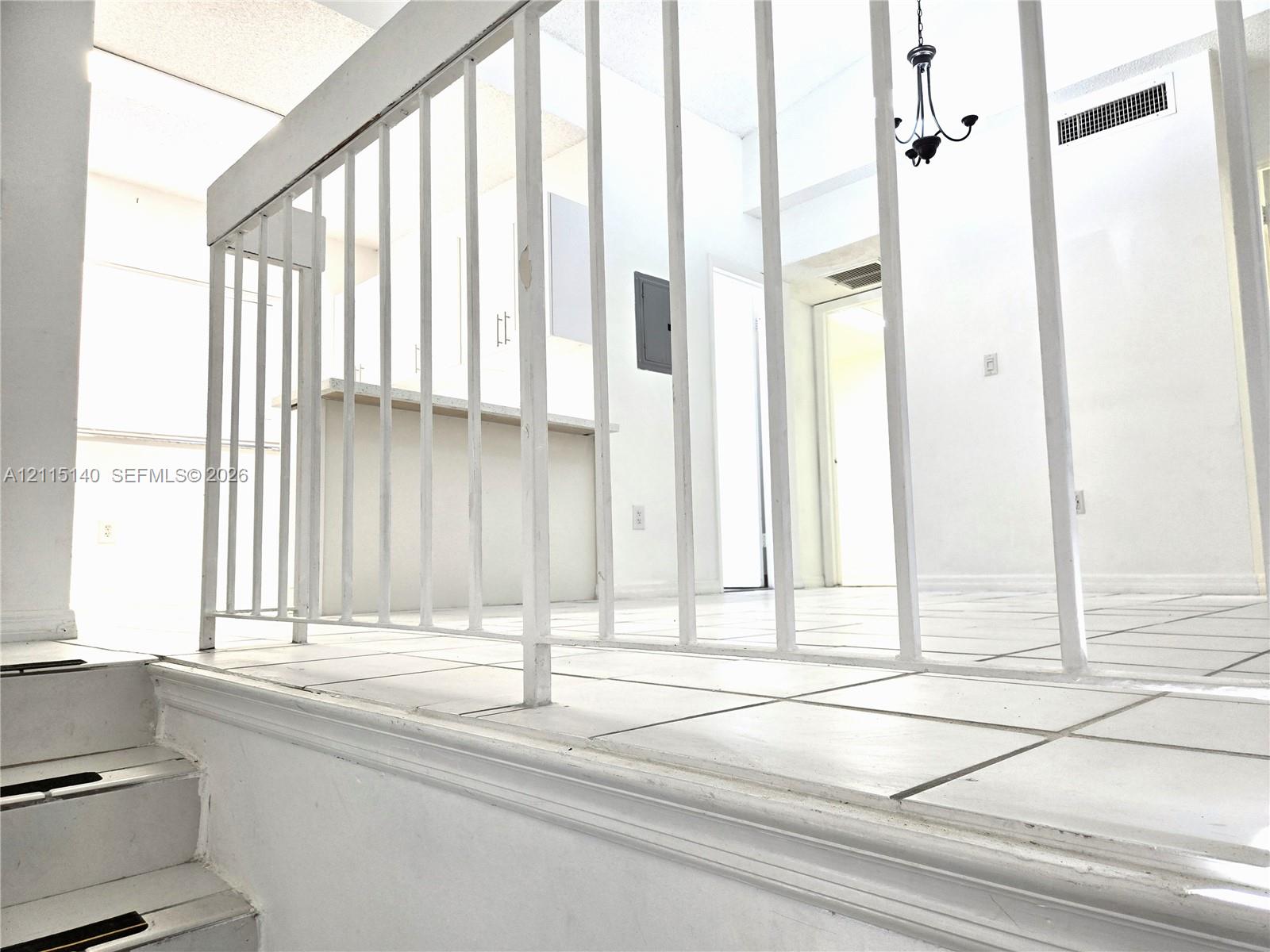 Raised platform level with white ceramic tile flooring, vertical metal railing, and overhead chandelier lighting