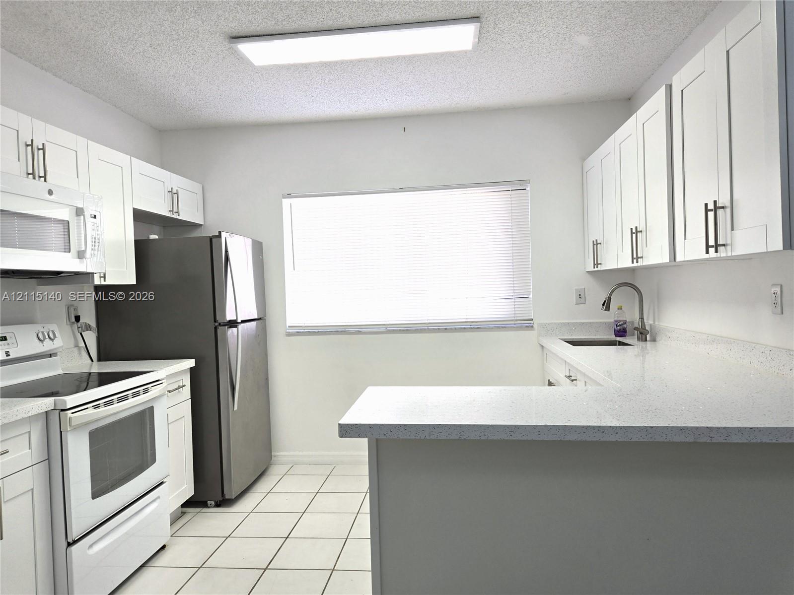 Kitchen featuring white shaker-style cabinetry, solid-surface countertops, tile flooring, stainless steel appliances, and a gooseneck faucet