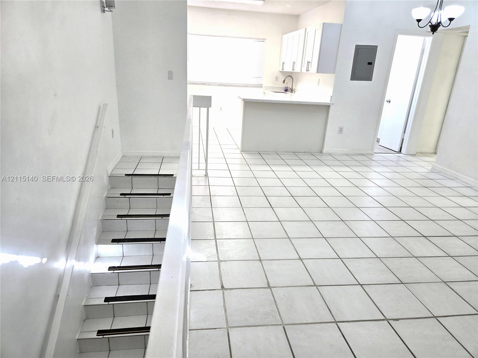 Open interior space featuring white ceramic tile flooring, kitchen cabinetry, peninsula counter, and tiled staircase with integrated tread detailing