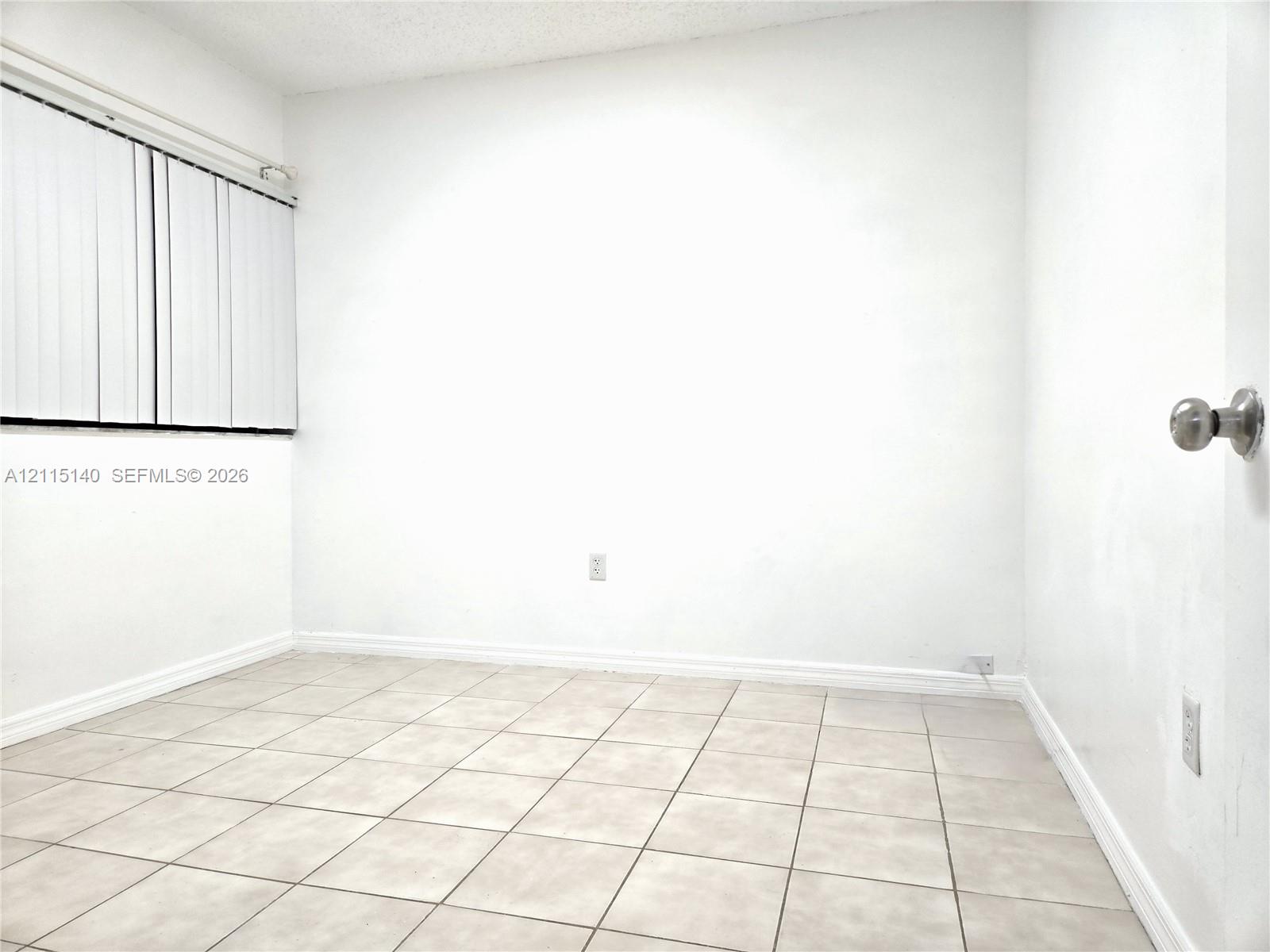 Room featuring ceramic tile flooring, vertical blind window treatments, and a metal door handle