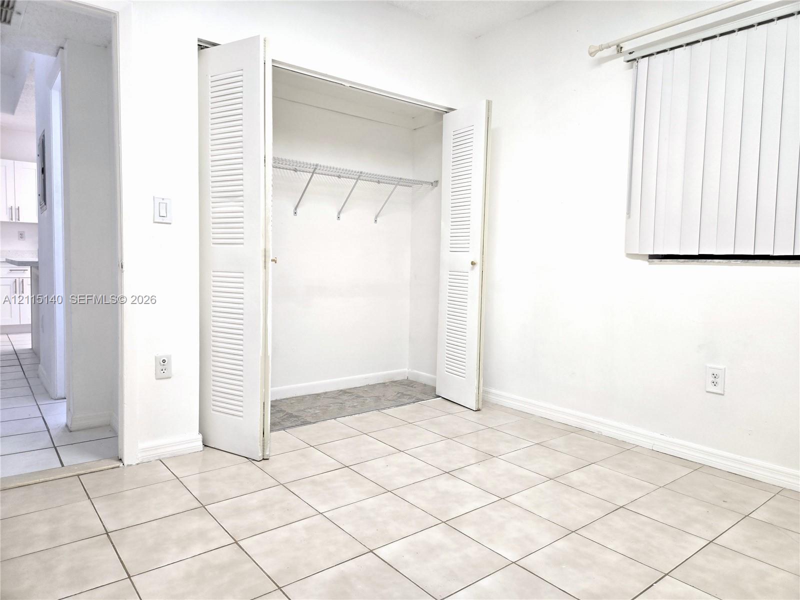 Room featuring ceramic tile flooring, closet with bi-fold louvered doors, and vertical window blinds