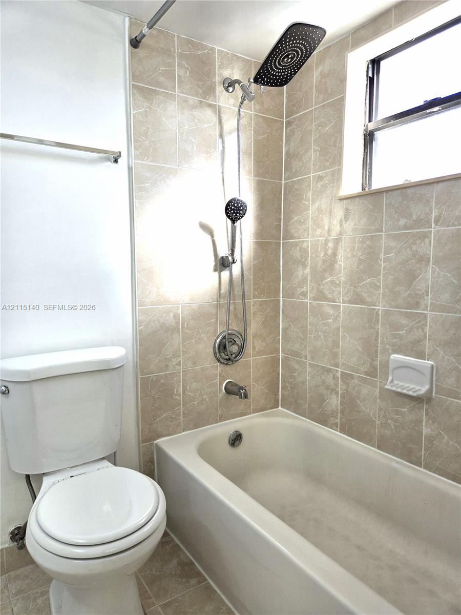 Bathroom featuring a porcelain tub, dual-head shower system with a rain-style fixture, neutral tile surround, integrated soap dish, and a window