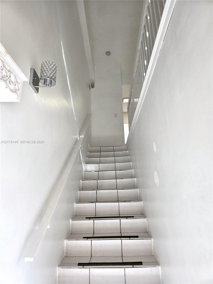 Staircase featuring white tile treads, a white handrail, decorative wall-mounted lighting, and a white balustrade
