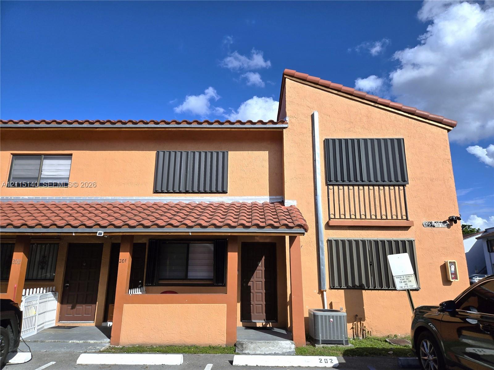 Two-story stucco exterior featuring a clay tile roof, decorative wrought iron balcony railing, and accordion-style storm shutters Two-story stucco exterior featuring a clay tile roof, decorative wrought iron balcony railing, and accordion-style storm shutters