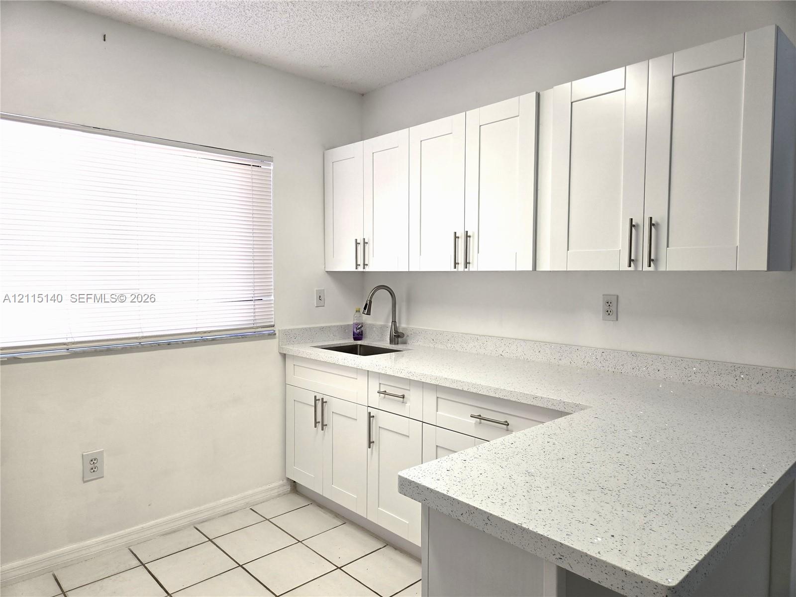 White Shaker-style cabinetry with satin nickel hardware, speckled quartz countertops, under-mount stainless steel sink, gooseneck faucet, and ceramic tile flooring