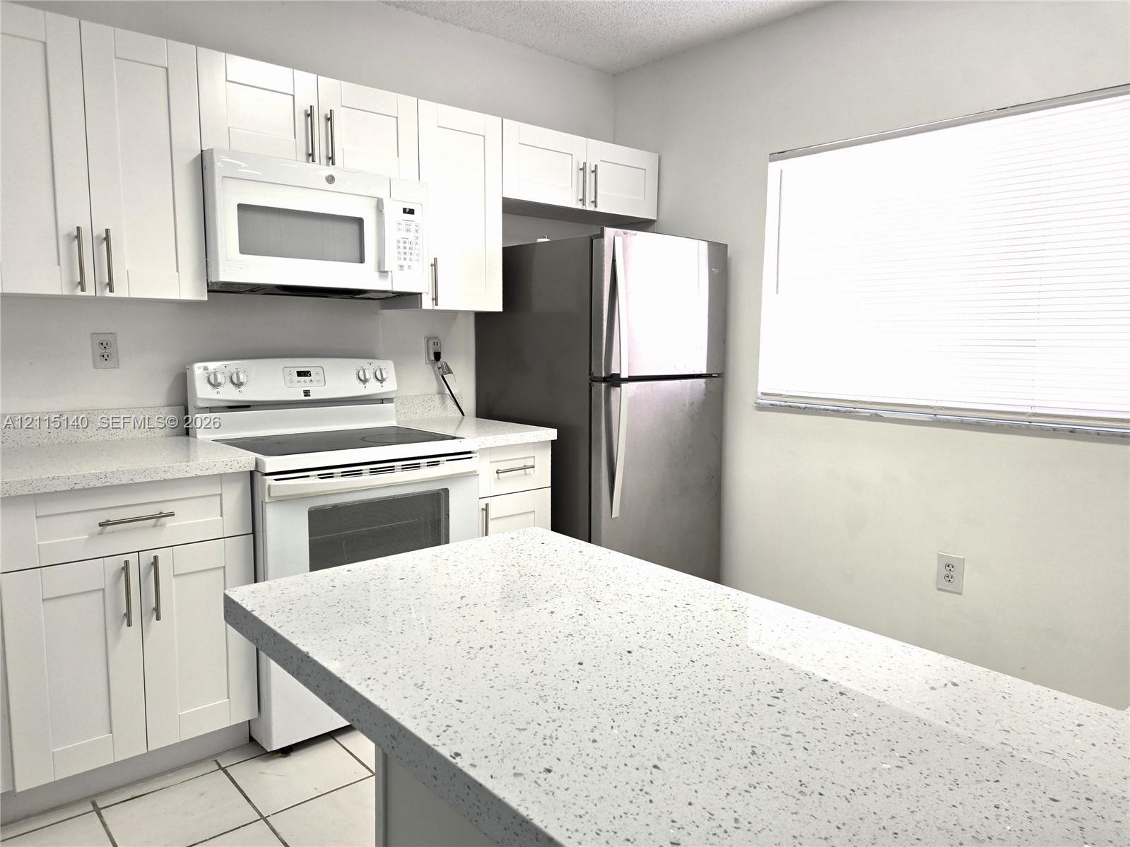 Kitchen featuring white shaker-style cabinetry, solid-surface countertops, a breakfast bar, and stainless steel appliances