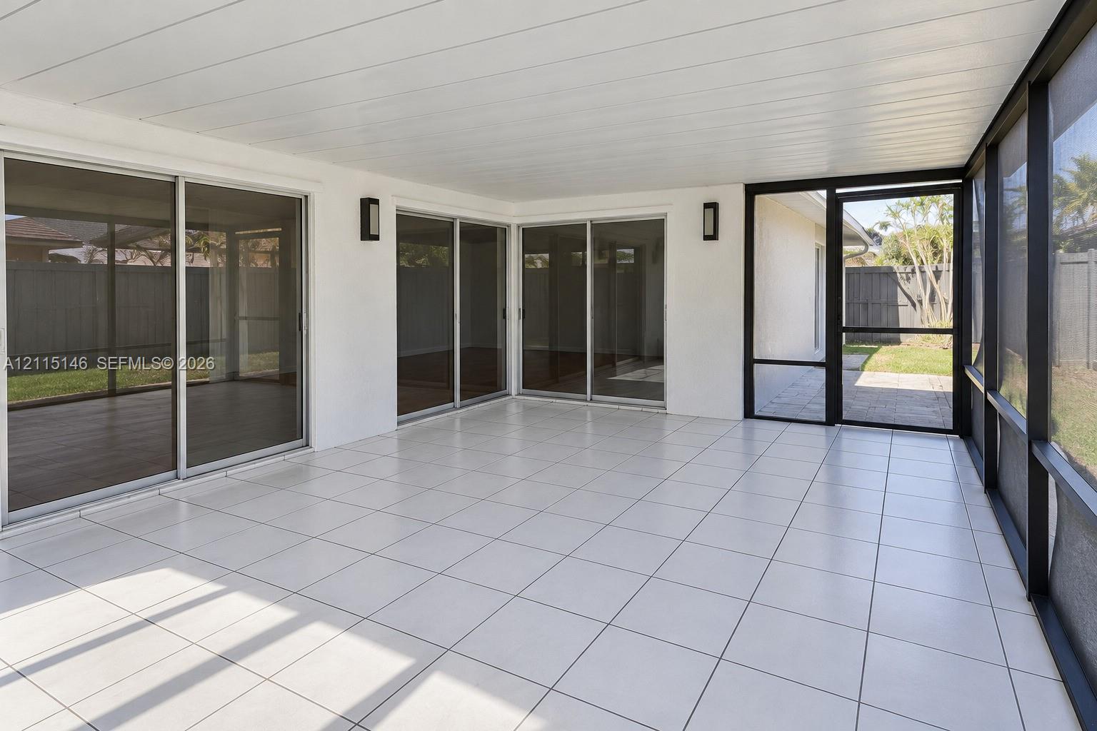 Screened-in patio featuring tile flooring, a paneled ceiling, dual wall-mounted light fixtures, and multiple sliding glass doors