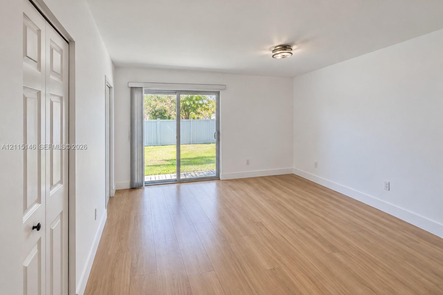 Neutral-toned interior featuring wood-finish flooring, sliding glass door, white walls, and built-in closet with paneled doors