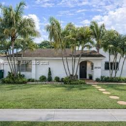 Single-story exterior featuring white stucco siding, a recessed arched entry, mature palm trees, and a stone paver walkway