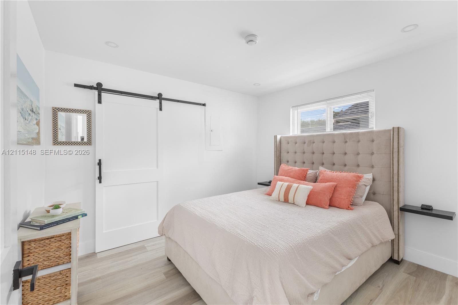 Room featuring wood-finish flooring, a white sliding barn door with matte black hardware, recessed lighting, and wall-mounted shelving