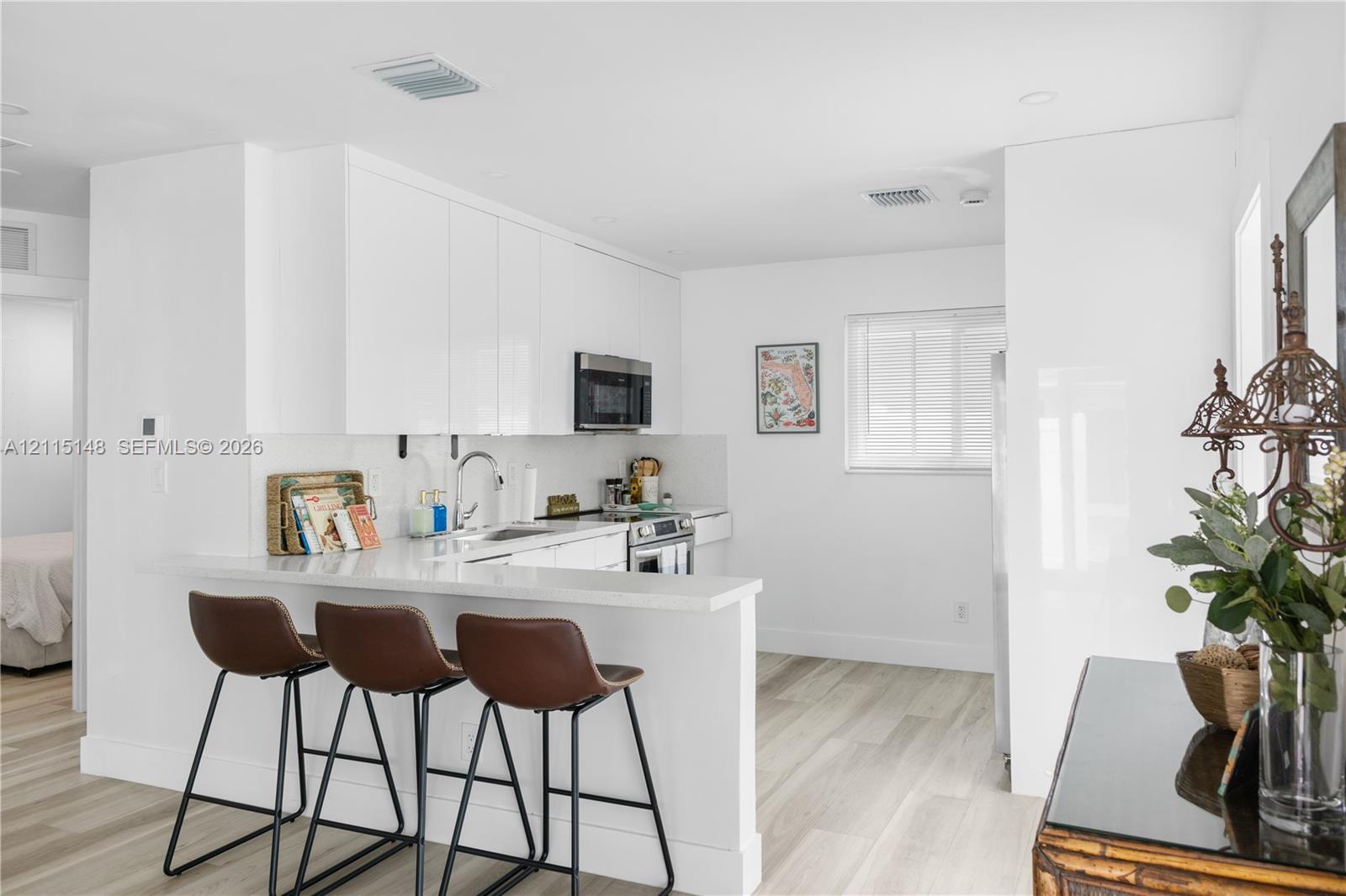 Kitchen featuring white high-gloss flat-panel cabinetry, a peninsula with a stone-surface countertop, stainless steel appliances, and wood-finish flooring