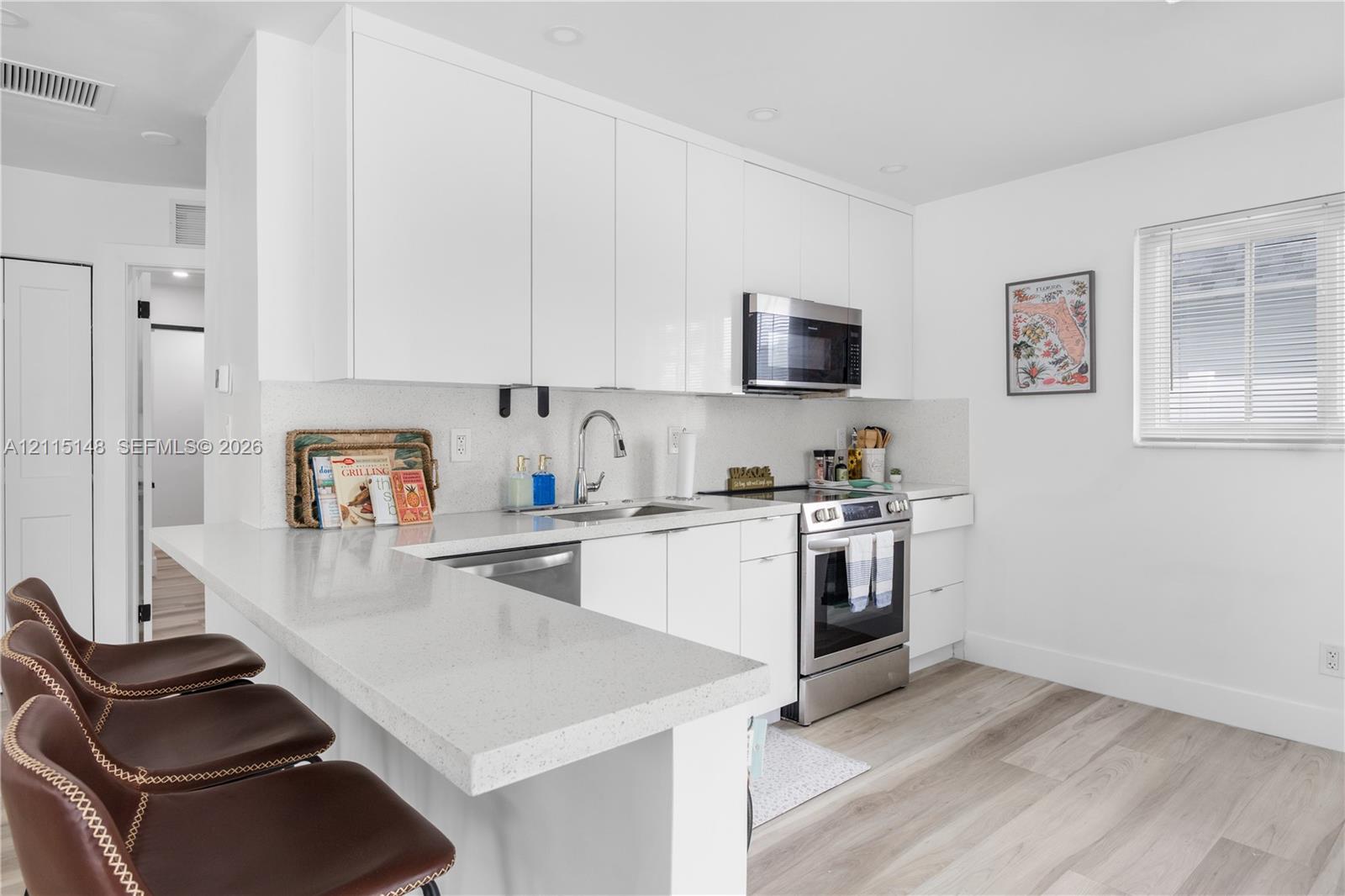 Kitchen featuring high-gloss white cabinetry, quartz countertops, a peninsula with bar seating, stainless steel appliances, and wood-finish flooring