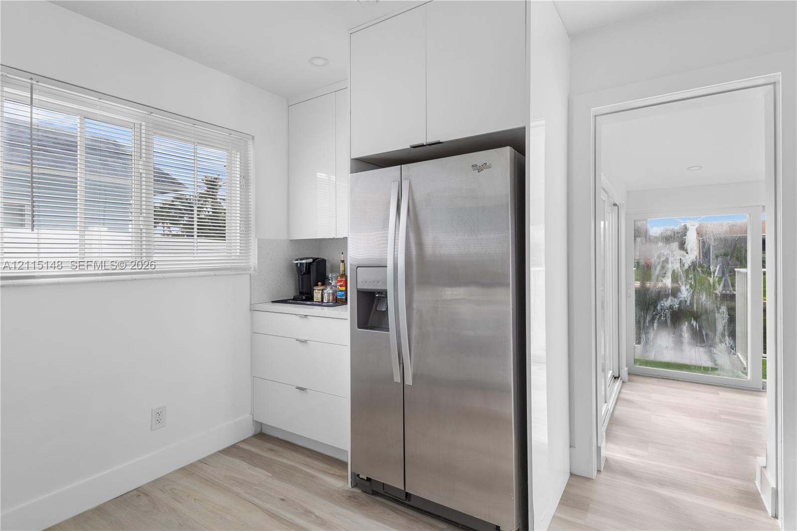 Glossy white flat-panel cabinetry, stainless steel refrigerator, horizontal window blinds, recessed ceiling lighting, and wood-finish flooring