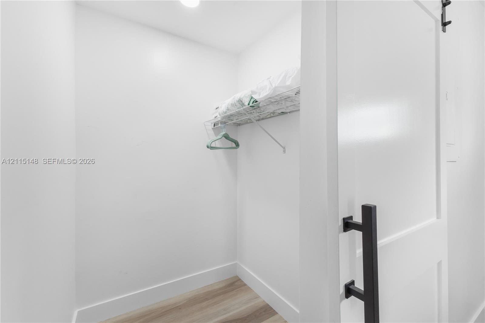Storage area featuring wood-finish flooring, white walls, and wire shelving with an integrated clothes rod, accessible via a door with a matte black handle