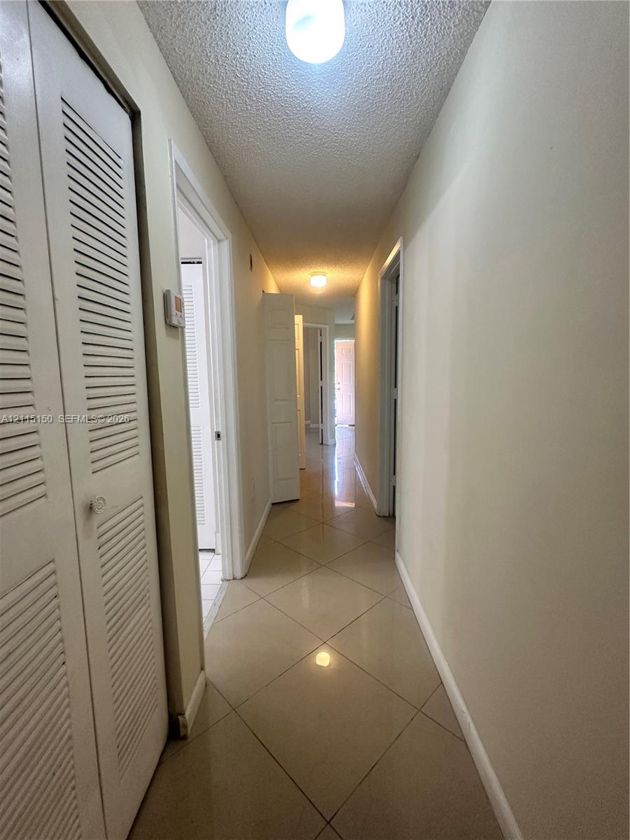 Hallway featuring neutral large-format tile flooring and louvered-style closet doors