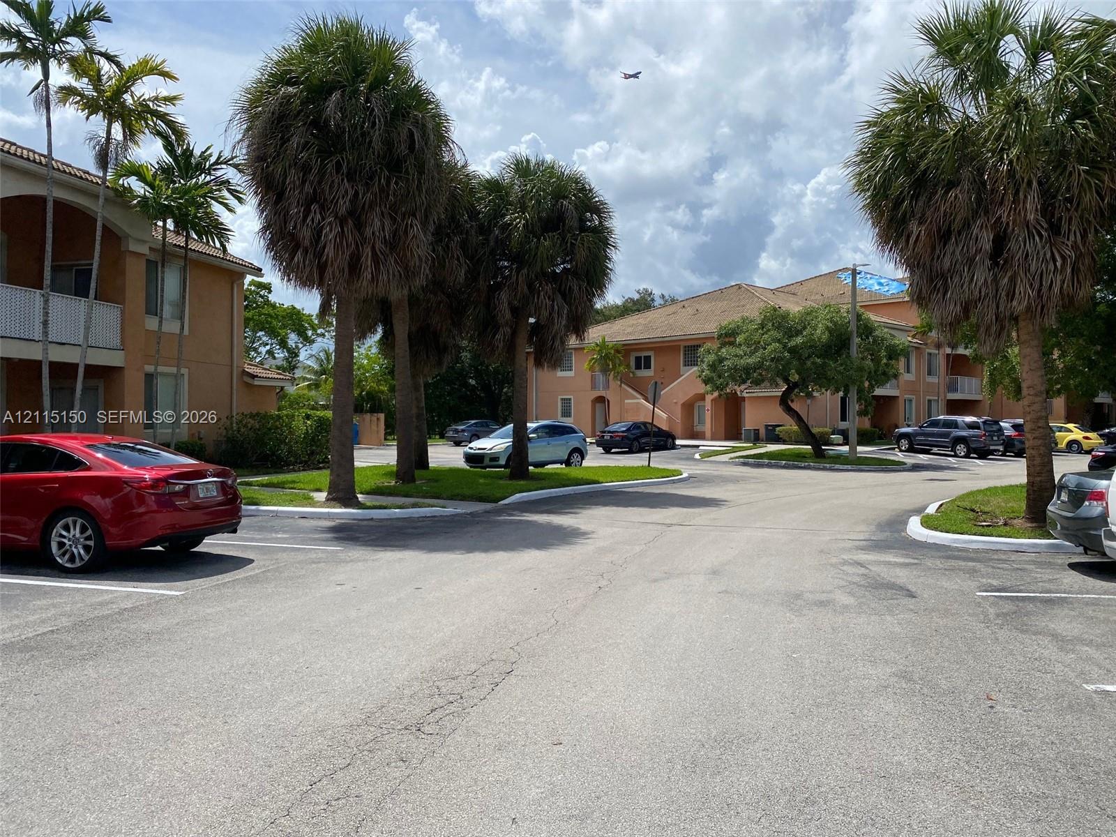 Stucco exterior multi-story buildings featuring tiled rooflines, designated asphalt parking areas, and landscaped grounds with mature palm trees