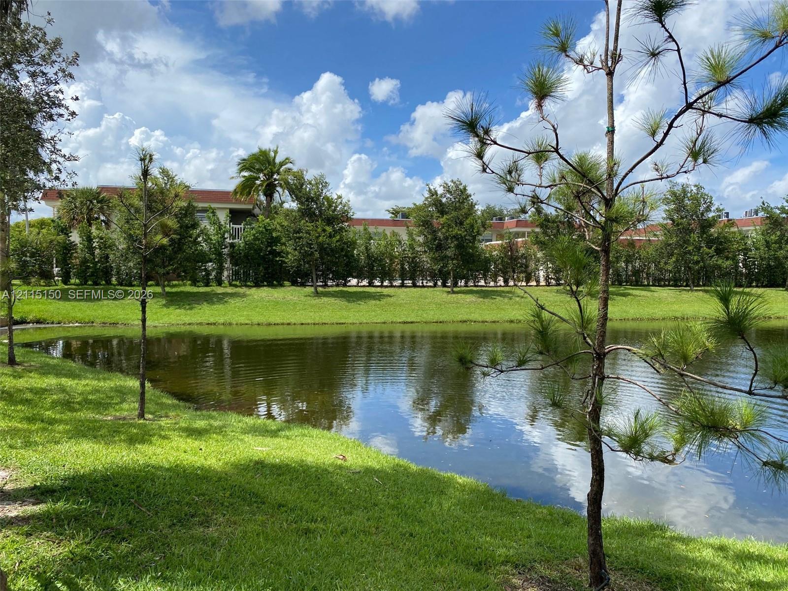 Waterfront property featuring a pond, manicured lawn, mature trees, and landscaping